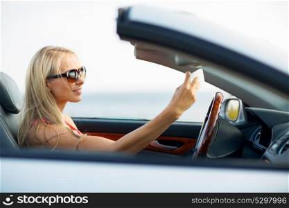 travel, road trip and people concept - happy young woman in convertible car taking selfie by smartphone. woman in convertible car taking selfie