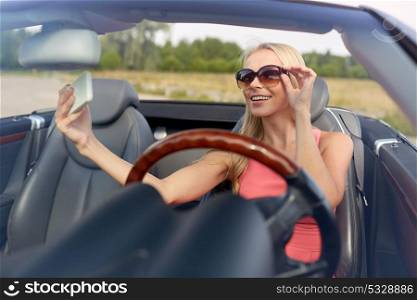 travel, road trip and people concept - happy young woman in convertible car taking selfie by smartphone. woman in convertible car taking selfie