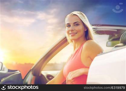 travel, road trip and people concept - happy young woman in convertible car over evening sky background. happy woman in convertible car over evening sky
