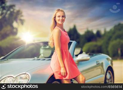 travel, road trip and people concept - happy young woman posing at convertible car over evening sky background. happy young woman posing at convertible car
