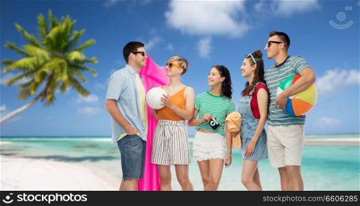 travel, summer holidays and tourism concept - group of happy smiling friends in sunglasses with ball, volleyball, towel, camera and floating mattress over tropical beach background in french polynesia. happy friends with beach and summer accessories
