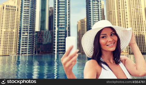 travel, summer, technology and people concept - sexy young woman taking selfie with smartphone over infinity edge pool in dubai city background