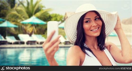 travel, summer, technology and people concept - sexy young woman taking selfie with smartphone over beach and swimming pool background