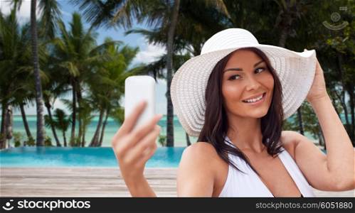 travel, summer, technology and people concept - sexy young woman taking selfie with smartphone over tropical beach with palms and swimming pool background