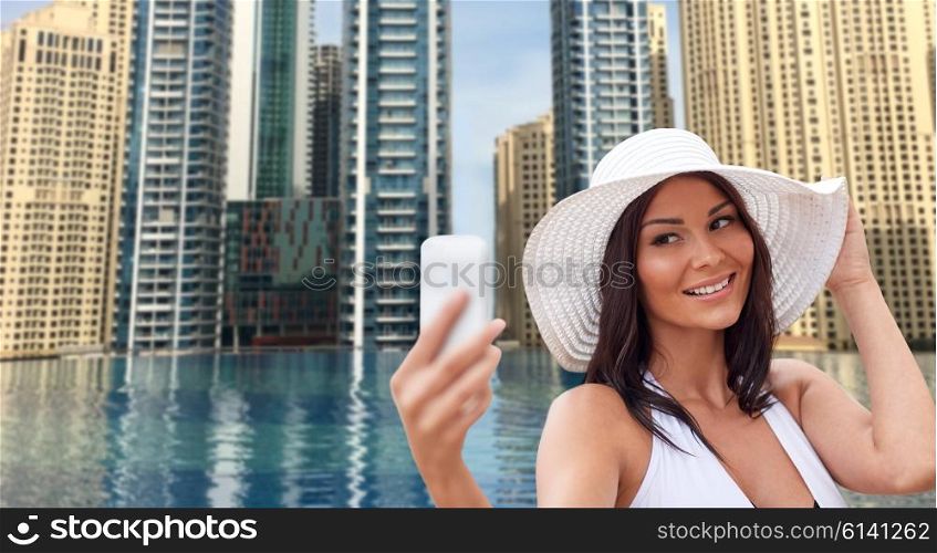 travel, summer, technology and people concept - sexy young woman taking selfie with smartphone over infinity edge pool in dubai city background