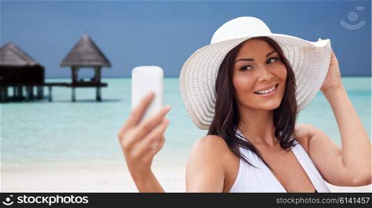 travel, summer, technology and people concept - sexy young woman taking selfie with smartphone over bungalow on beach background