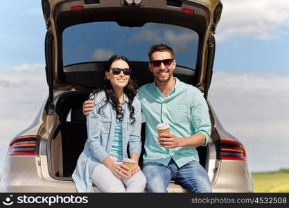 travel, summer vacation, road trip, leisure and people concept - happy couple drinking coffee from disposable cups sitting on trunk of hatchback car outdoors