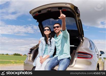 travel, summer vacation, road trip, leisure and people concept - happy couple hugging at open trunk of hatchback car and pointing finger outdoors