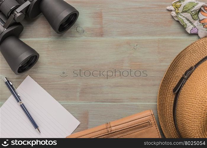 Travel, summer vacation, tourism and objects concept - close up of binoculars, hat, pen, paper and scarf on wooden table. Top view with copy space.