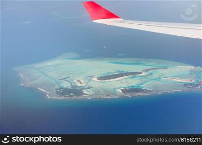 travel, summer vacation, transportation, air transport and vehicle concept - close up of airplane wing flying above Maldive island in ocean