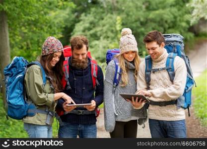 travel, technology and hiking concept - group of smiling friends or travelers with backpacks and tablet pc computers outdoors. friends or travelers with backpacks and tablet pc