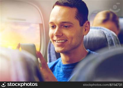 travel, tourism and air flights concept - close up of happy young man sitting in plane with smartphone over porthole background. happy man sitting in plane with smartphone. happy man sitting in plane with smartphone
