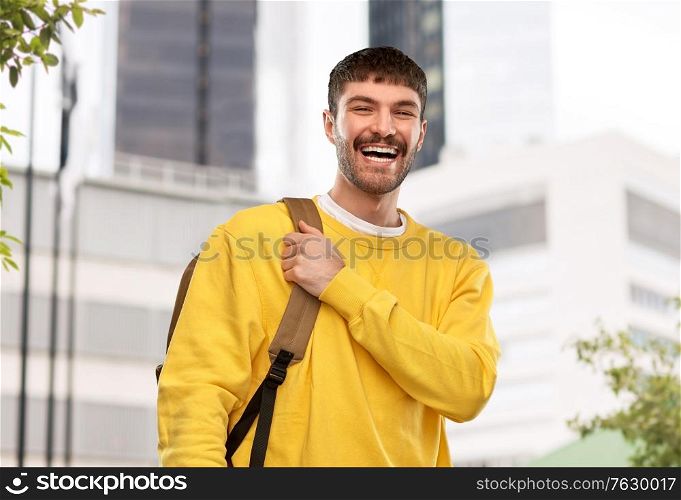 travel, tourism and education concept - happy smiling young man with backpack over city background. happy smiling young man with backpack in city