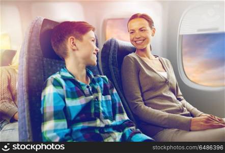 travel, tourism and family concept - happy mother and son sitting in plane and talking over porthole background. happy mother and son traveling by plane. happy mother and son traveling by plane