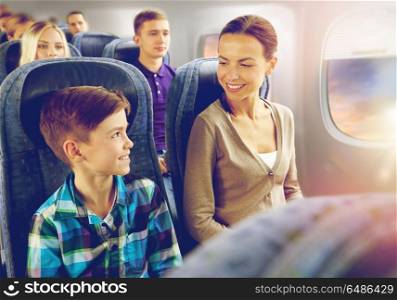 travel, tourism and family concept - happy mother and son sitting in plane and talking over porthole background. happy mother and son traveling by plane. happy mother and son traveling by plane