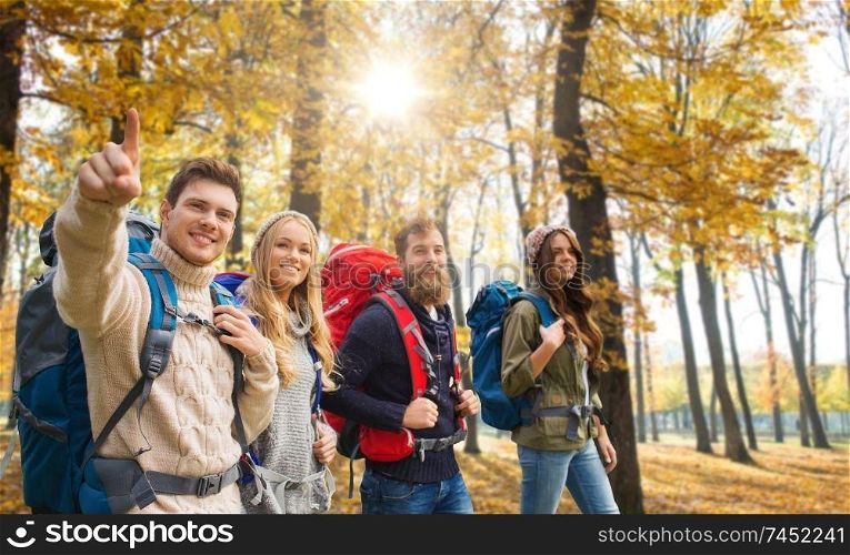 travel, tourism and hike concept - group of smiling friends walking with backpacks over autumn park background. friends with backpacks hiking in autumn