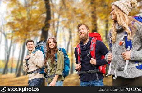 travel, tourism and hike concept - group of smiling friends walking with backpacks over autumn park background. friends with backpacks hiking in autumn