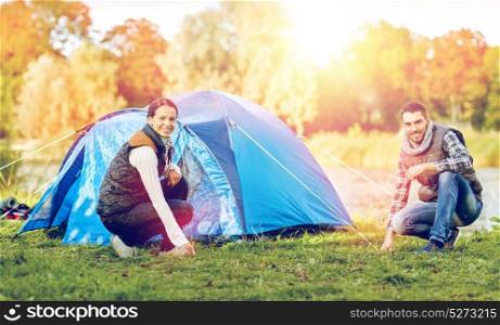 travel, tourism and hike concept - happy couple setting up tent outdoors. happy couple setting up tent outdoors