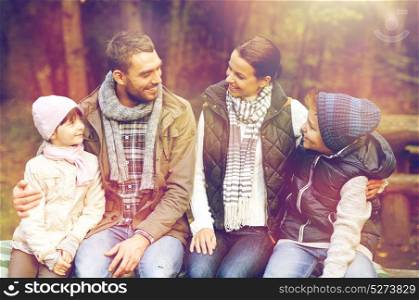travel, tourism and hike concept - happy family sitting on bench and talking at camp in woods. happy family sitting on bench and talking at camp