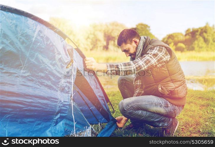 travel, tourism and hike concept - happy male traveler setting tent up outdoors. happy male traveler setting tent up outdoors