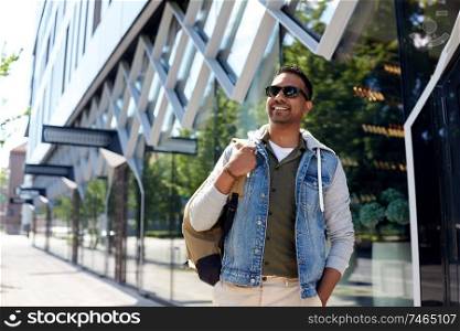 travel, tourism and lifestyle concept - smiling indian man with backpack walking along city street. indian man with backpack walking along city street