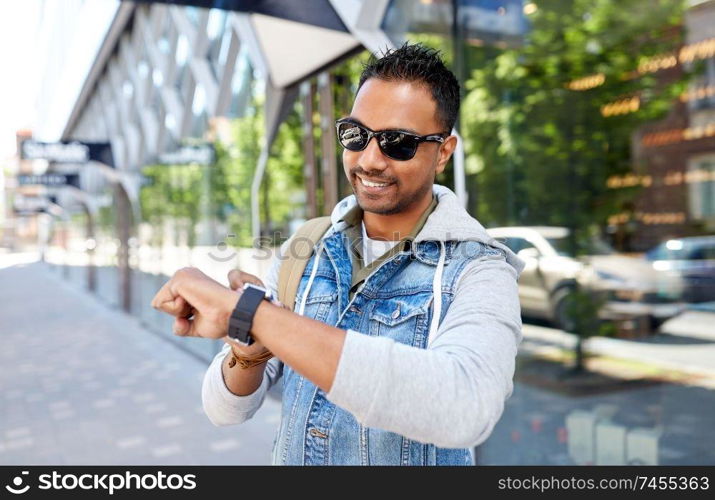 travel, tourism and lifestyle concept - smiling indian man with smart watch and backpack walking along city street. indian man with smart watch and backpack in city