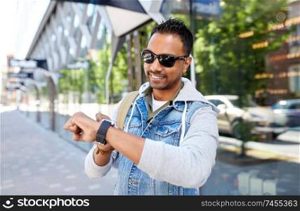 travel, tourism and lifestyle concept - smiling indian man with smart watch and backpack walking along city street. indian man with smart watch and backpack in city