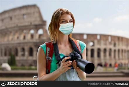 travel, tourism and pandemic concept - young woman with backpack and camera wearing protective medical mask for protection from virus disease over coliseum in rome, italy background. happy woman with backpack and camera outdoors