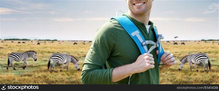 travel, tourism and people concept - close up of happy young man with backpack over african savannah and zebras background. close up of happy man with backpack traveling