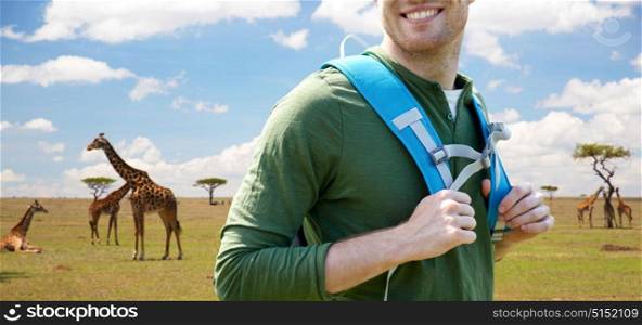 travel, tourism and people concept - close up of happy young man with backpack over african savannah and giraffes background. close up of happy man with backpack traveling