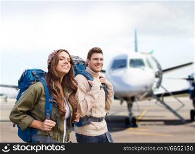 travel, tourism and people concept - couple of tourists with backpacks over plane on airfield background. couple of tourists with backpacks over plane