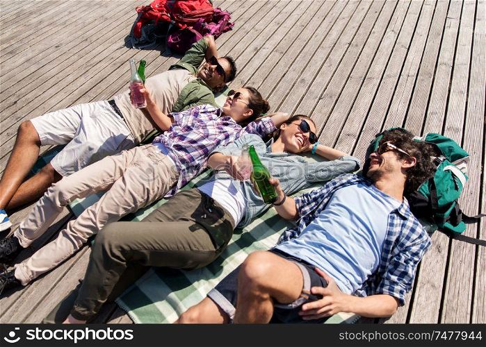 travel, tourism and people concept - friends drinking beer and cider on wooden terrace in summer. friends drinking beer and cider on wooden terrace