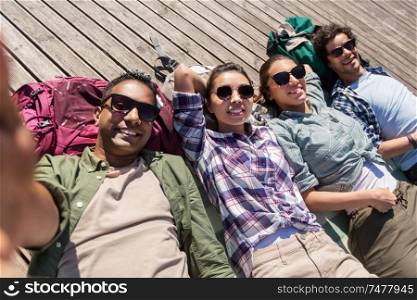 travel, tourism and people concept - group of friends or tourists with backpacks lying on wooden terrace and taking selfie. friends or tourists with backpacks taking selfie