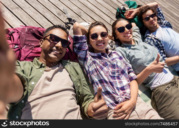 travel, tourism and people concept - group of friends or tourists with backpacks lying on wooden terrace and taking selfie. friends or tourists with backpacks taking selfie