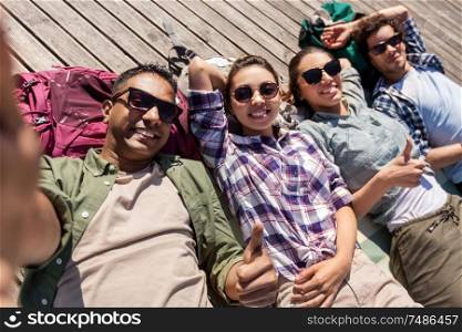 travel, tourism and people concept - group of friends or tourists with backpacks lying on wooden terrace and taking selfie. friends or tourists with backpacks taking selfie