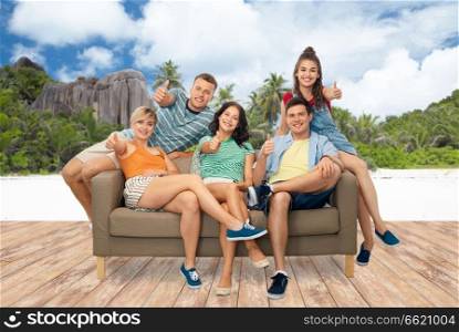 travel, tourism and people concept - group of happy smiling friends sitting on sofa and showing thumbs up over tropical beach on seychelles island background. friends showing thumbs up over seychelles island 