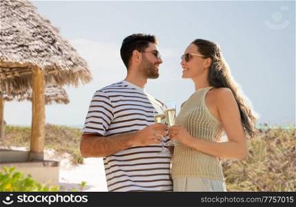 travel, tourism and people concept - happy couple in sunglasses drinking champagne over tropical beach background in french polynesia. happy couple drinking champagne on summer beach