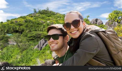 travel, tourism and people concept - happy couple in sunglasses with backpacks over natural exotic island background. happy couple with backpacks traveling