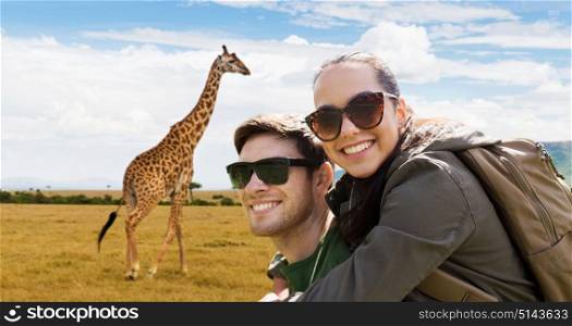 travel, tourism and people concept - happy couple in sunglasses with backpacks over african savannah and giraffe background. happy couple with backpacks traveling in africa