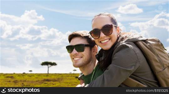 travel, tourism and people concept - happy couple in sunglasses with backpacks traveling over african savannah background. happy couple with backpacks traveling in africa