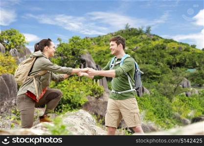 travel, tourism and people concept - happy couple with backpacks climbing over fallen tree trunk over exotic island hills background. couple with backpacks traveling over exotic island