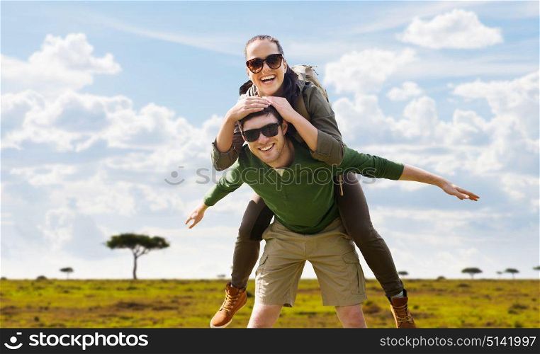 travel, tourism and people concept - happy couple with backpacks having fun over african savannah background. smiling couple with backpacks traveling in africa