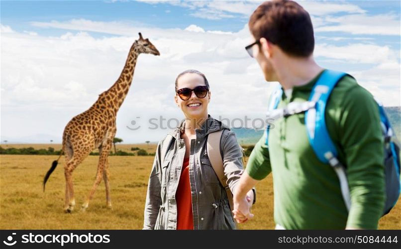 travel, tourism and people concept - happy couple with backpacks holding hands over african savannah and giraffe background. smiling couple with backpacks traveling in africa. smiling couple with backpacks traveling in africa