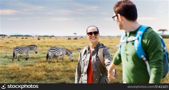 travel, tourism and people concept - happy couple with backpacks holding hands over african savannah and zebras background. smiling couple with backpacks traveling in africa