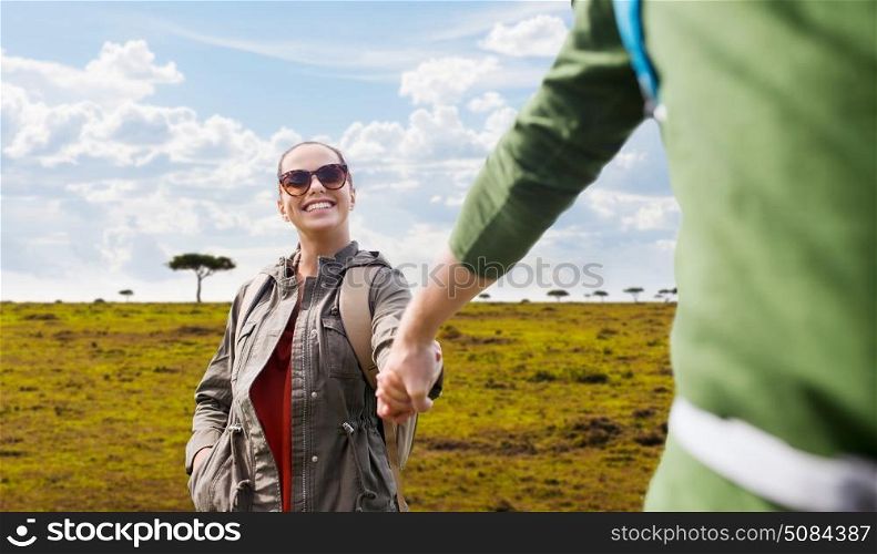 travel, tourism and people concept - happy couple with backpacks holding hands over african savannah background. happy couple with backpacks traveling in africa. happy couple with backpacks traveling in africa
