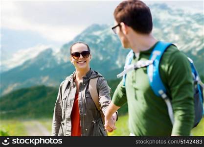 travel, tourism and people concept - happy couple with backpacks holding hands over alps mountains background. happy couple with backpacks traveling in highlands