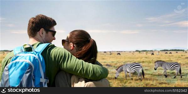 travel, tourism and people concept - happy couple with backpacks hugging over african savannah and zebras background. happy couple with backpacks traveling