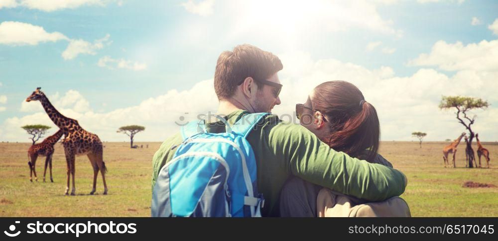 travel, tourism and people concept - happy couple with backpacks hugging over african savannah and giraffes background. happy couple with backpacks traveling. happy couple with backpacks traveling