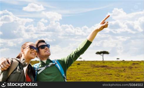travel, tourism and people concept - happy couple with backpacks outdoors pointing finger to something over african savannah background. happy couple with backpacks traveling in africa. happy couple with backpacks traveling in africa
