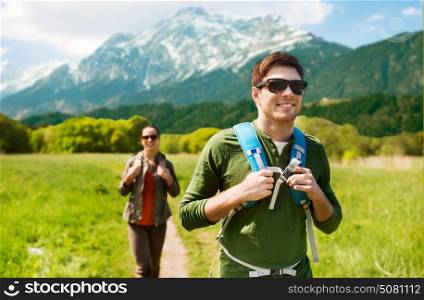 travel, tourism and people concept - happy couple with backpacks walking along country road over mountains background. happy couple with backpacks hiking outdoors